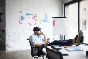 Thoughtful businessman holding disposable cup while sitting at creative office - CAVF29509