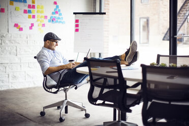 Smiling businessman sitting on chair at creative office - CAVF29510