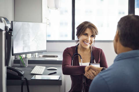 Glückliche Ärztin schüttelt Hände mit männlichem Patienten in der Klinik, lizenzfreies Stockfoto