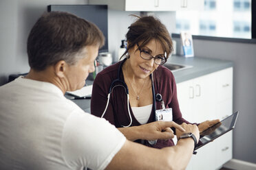 Männlicher Patient, der auf seine Armbanduhr zeigt, während er mit einer Ärztin in der Klinik spricht - CAVF29532