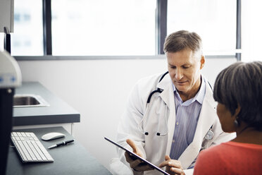 Männlicher Arzt zeigt einem Patienten in der Klinik einen Bericht auf einem Tablet-Computer - CAVF29538