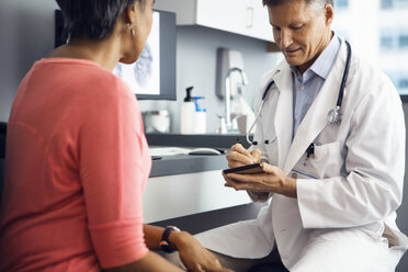 Male doctor writing in note pad while sitting with female patient in clinic - CAVF29540