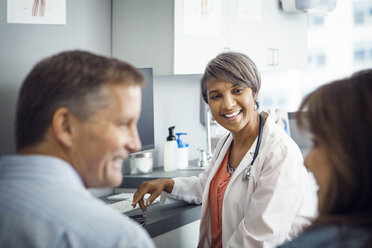 Happy female doctor looking at couple in clinic - CAVF29541