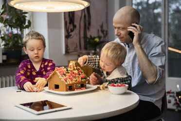 Mann und zwei Jungen dekorieren ein Lebkuchenhaus - FOLF01848
