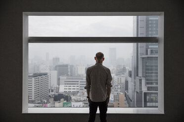 Mann schaut durch ein Fenster auf eine Stadtlandschaft - FOLF01866