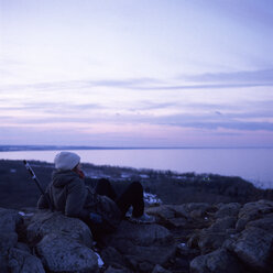 Frau sitzt auf Steinen und beobachtet das Meer - FOLF01998