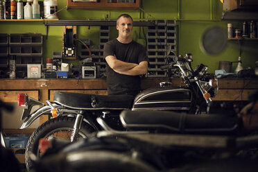 Porträt eines selbstbewussten Besitzers, der in einer Werkstatt neben einem Motorrad steht - CAVF29579