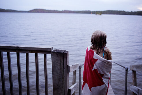 Rear view of girl wrapped in towel standing on jetty over lake - CAVF29587