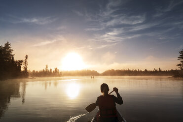 Rückansicht einer Frau, die in einem Boot auf einem ruhigen See gegen den Himmel fährt - CAVF29596