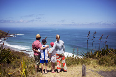 Rear view of family standing on hill and looking at sea against sky - CAVF29606