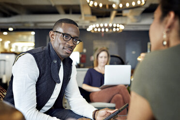 Business people talking with female colleague using laptop computer in background at creative office - CAVF29682