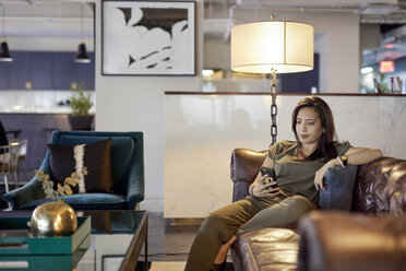 Geschäftsfrau, die ein Smartphone benutzt, während sie auf dem Sofa im Kreativbüro sitzt - CAVF29692