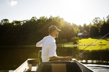 Man fishing while sitting in rowboat on lake during sunny day - CAVF29710