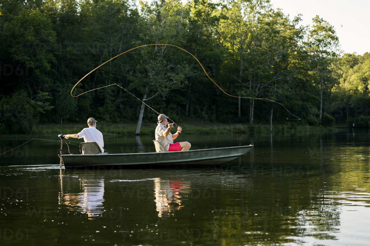 Man casting fishing line in lake with friend sitting in rowboat stock photo