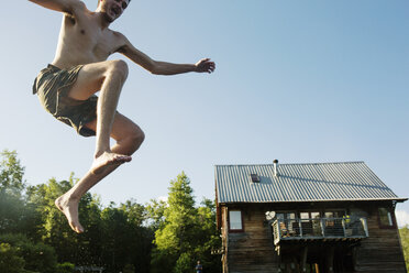 Niedriger Blickwinkel von hemdsärmeligen Mann springt in den See gegen Blockhaus und klaren Himmel - CAVF29717