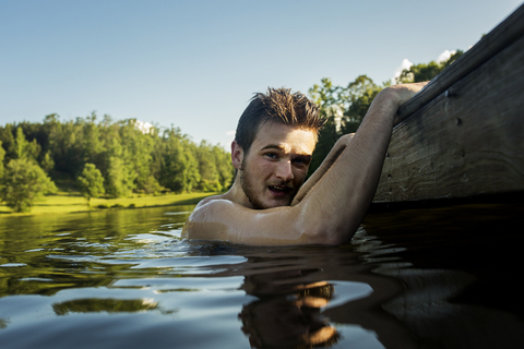 Porträt eines im See schwimmenden Mannes ohne Hemd vor Bäumen und klarem Himmel, lizenzfreies Stockfoto