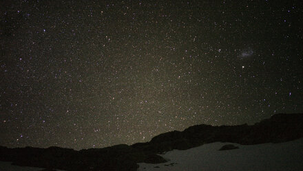 Landschaftliche Ansicht eines schneebedeckten Feldes vor einem nächtlichen Sternenfeld - CAVF29740