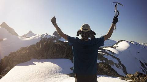 Rückansicht eines Mannes, der mit erhobenen Armen auf einem schneebedeckten Berg steht, lizenzfreies Stockfoto