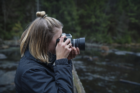 Side view of woman photographing with camera against river stock photo