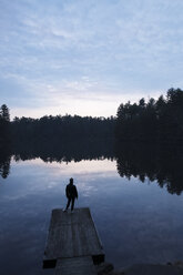 Rear view of woman standing on pier at lake against sky - CAVF29763