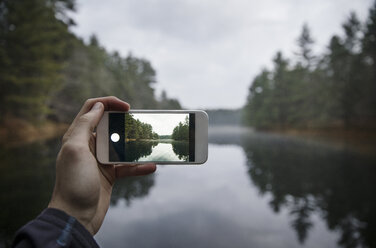 Ausgeschnittenes Bild einer Hand, die mit einem Smartphone einen See fotografiert - CAVF29765