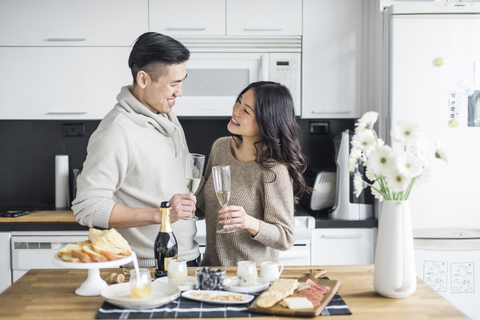 Glückliches Paar mit Getränken, die sich gegenseitig ansehen, während sie zu Hause in der Küche stehen, lizenzfreies Stockfoto