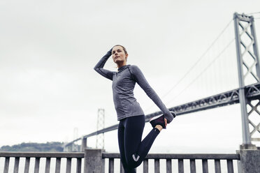 Side view of determined female athlete stretching leg with Oakland Bay Bridge in background - CAVF29810