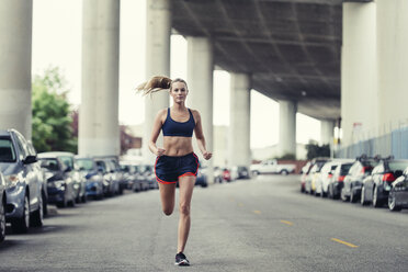 Full length of determined female athlete running on street under bridge - CAVF29812