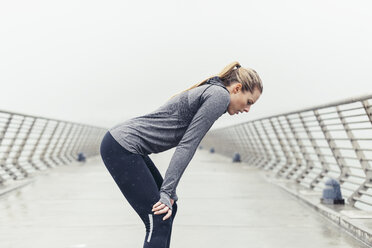 Seitenansicht einer müden Sportlerin, die mit den Händen auf den Knien auf einer Brücke gegen den klaren Himmel steht - CAVF29816