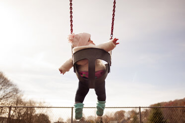 Low angle view of baby girl sitting on swing at park - CAVF29856