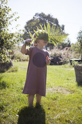 Mädchen steht im Garten und hält ein Farnblatt - FOLF02100