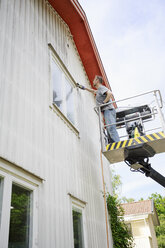 Man in cherry picker cleaning wall of house - FOLF02107