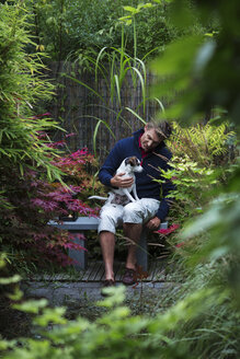 Mann sitzt mit Hund auf einer Bank im japanischen Garten - FOLF02136