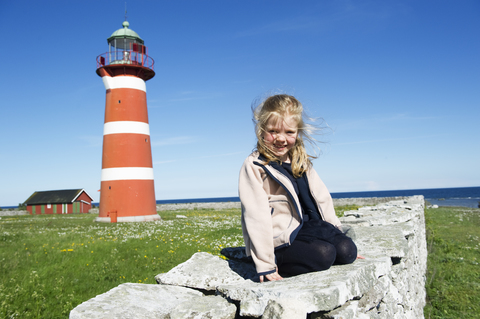 Mädchen sitzt auf einem Felsen mit Leuchtturm im Hintergrund, lizenzfreies Stockfoto