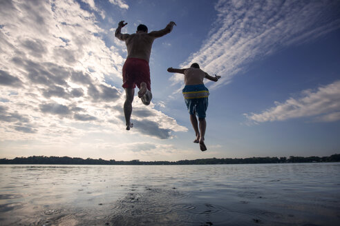 Niedriger Blickwinkel von Vater und Sohn, die gegen den Himmel in den See springen - CAVF29883