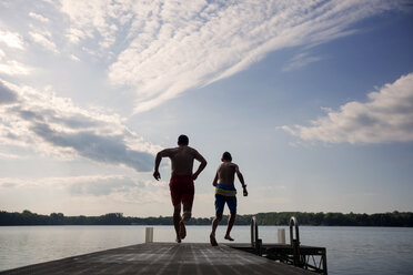 Rear view of father and son running on pier at lake - CAVF29885