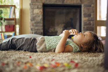 Mädchen isst Essen, während sie auf dem Teppich zu Hause liegt - CAVF29891