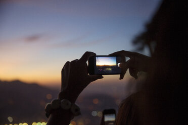 Woman photographing illuminated cityscape with smart phone during sunset - CAVF29893