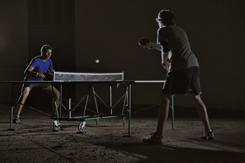 Freunde spielen Tischtennis gegen ein Gebäude bei Nacht, lizenzfreies Stockfoto