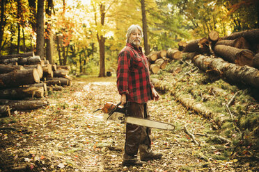 Side view portrait of confident lumberjack holding chainsaw in forest - CAVF29938