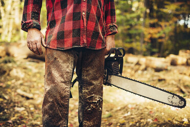 Midsection of lumberjack holding chainsaw in forest - CAVF29940