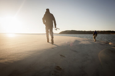 Rückansicht von Männern, die eine Angelrute halten, während sie bei Sonnenuntergang über den Sand laufen - CAVF30009