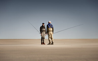 Freunde halten Angelruten, während sie auf Sand gegen den klaren Himmel stehen - CAVF30014