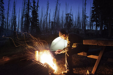 Mann sitzt am Lagerfeuer auf einem Feld - CAVF30025