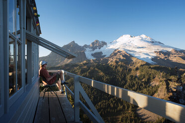 Seitenansicht eines Mannes, der auf dem Balkon eines Ferienhauses sitzt und die Berge sieht - CAVF30031