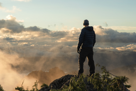 Rückansicht eines auf einer Klippe stehenden Mannes gegen einen bewölkten Himmel, lizenzfreies Stockfoto