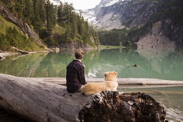 Rear view of man and dog sitting on fallen tree at Blanca Lake - CAVF30062