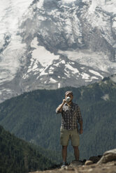 Mann trinkt Kaffee, während er auf Felsen vor Bergen steht - CAVF30097