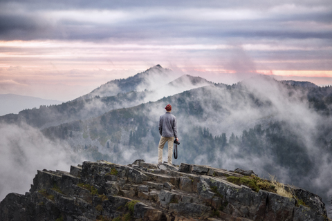 Rückansicht des auf einer Klippe stehenden Fotografen vor bewölktem Himmel, lizenzfreies Stockfoto