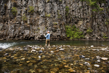 Rear view of man fly fishing at river against rock formations - CAVF30118